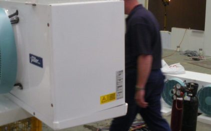 man in a blue shirt standing behind a piece of industrial refrigeration equipment